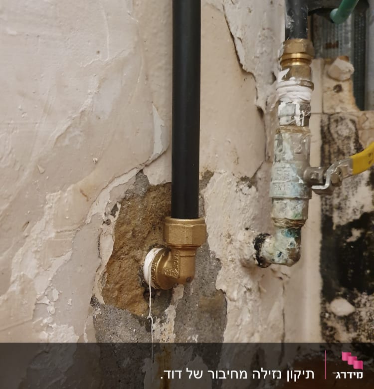 צינור שחור עם חיבורי מתכת על קיר מתקלף